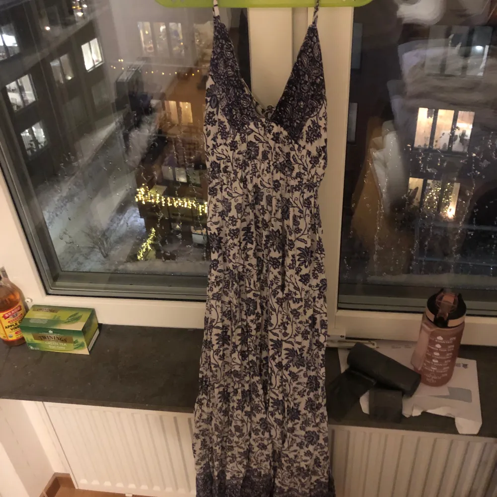Säljer en vacker långklänning med blommigt mönster i blått och vitt. Klänningen har en öppen rygg och smala axelband, perfekt för sommarens varma dagar. Den har en omlott-design framtill som ger en fin passform. PERFEKT TILL SOMMAREN 💗i storlek M men passar S bättre då den är liten . Mekot.