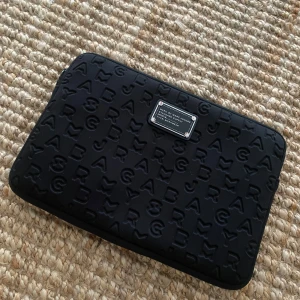 Marc Jacobs datorfodral svart - Svart datorfodral från Marc Jacobs i mycket bra skick!  Det ända som har defekter är dragkedjan då den svarta färgen gått bort lite samt de fyra små ”spikarna” på kanten av plattan, annars inga defekter alls och i mycket bra skick!  I allmän har själva datorfodralet varken fläckar eller slitningar  Passar till 13 tum laptop och har måtten 32 x 22 cm