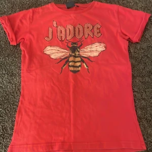 Röd t-shirt med bi och text från Petit Sofie Schnoor - Cool röd t-shirt från Petit Sofie Schnoor med ett stort bi och texten 'j'adore' på framsidan. Perfekt för en trendig look med en färgstark touch.