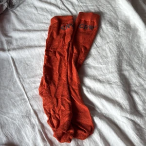 Orange rid strumpor från CRW - Säljer ett par knalliga orange ridstrumpor från CRW. Perfekta för att liva upp vilken outfit som helst. De är långa och har en enkel design med märkets logga upptill.
