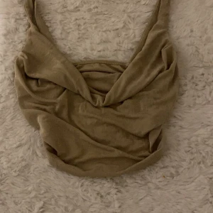 Beige omlottlinne - Snyggt beige omlottlinne med djup v-ringning och breda axelband. Perfekt för en stilren och avslappnad look.