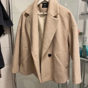 Beige kappa från Lindex - Säljer en stilren beige kappa från Lindex i storlek XS. Jackan har en klassisk design med knappar framtill och två fickor. Oversized storlek 