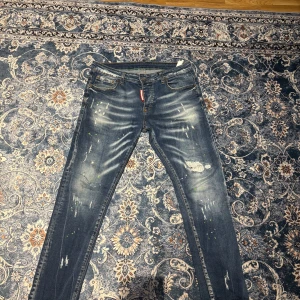 Blå jeans från Dsquared2 - Snygga blå jeans från Dsquared2 med slitna detaljer och en cool tvätt. De har en klassisk femficksdesign och en röd logga vid gylfen. Perfekta för en avslappnad stil.