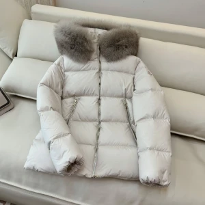 Vit dunjacka med pälskrage från Moncler - Snygg vit dunjacka från Moncler med en lyxig grå pälskrage. Jackan har dragkedja och knappar framtill samt två praktiska fickor med dragkedja. Perfekt för kalla vinterdagar. Jackan kommer levereras med orginalkvitto.