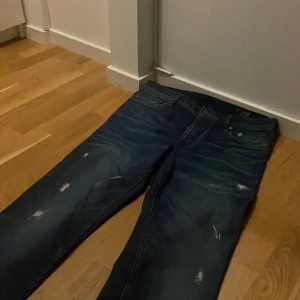 Mörkblå jeans från Jack & Jones - Snygga mörkblå jeans från Jack & Jones med en klassisk femficksdesign. Jeansen har en lätt slitning för en trendig look och är perfekta för vardagsbruk. De har en normal passform och är tillverkade i ett bekvämt denimtyg.