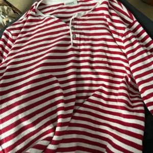 Röd- och vitrandig tröja från Dobber - Snygg röd- och vitrandig tröja från Dobber med knappar framtill. Perfekt för en avslappnad stil. Tillverkad i ett bekvämt material som passar bra till vardags. Djur finns i hushållet finns i Karlskrona 🤗