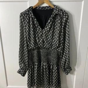 Mönstrad klänning från Zara - Snygg mönstrad klänning från Zara med smockdetaljer i midjan. Klänningen har långa ärmar och en v-ringad hals. Perfekt för både vardag och fest! Denna klänning är i storlek Xl men passar även M och L