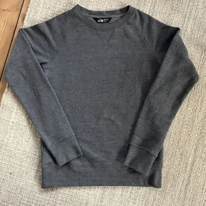 Basic Grå tröja från The North Face - Säljer en stilren grå tröja från The North Face. Tröjan har en klassisk design med rund hals och långa ärmar. Perfekt för en avslappnad look.