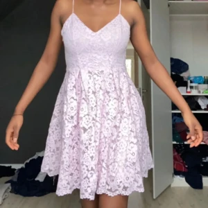 Ljusrosa spetsklänning - Charmig ljusrosa klänning i spets med smala axelband och v-ringad hals. Perfekt för sommarens festligheter med sin korta längd och romantiska stil.