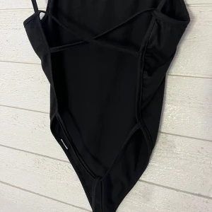 Svart body med snörning - Snygg svart body med smala axelband och trendig snörning på sidorna. Perfekt för en stilren look. Öppen rygg