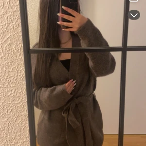 Brun stickad kofta med knytband - Mysig brun stickad kofta med knytband i midjan. Populär och slutsåld 