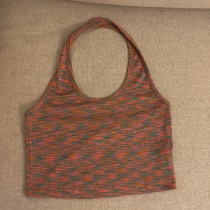 Flerfärgad ribbad linnetopp från H&M Divided - Säljer en cool flerfärgad ribbad linnetopp från H&M Divided. Toppen har ett mönster i orange, rosa och grönt och är ärmlös med en halterneck-design. Perfekt för en färgglad look!