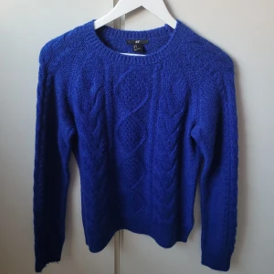 Blå stickad tröja från H&M - Säljer en snygg blå stickad tröja från H&M i storlek S. Den har ett klassiskt flätmönster och är perfekt för kyliga dagar. Tröjan är långärmad och supermjuk, vilket gör den både bekväm och stilren. Perfekt för höst och vinter! 💙