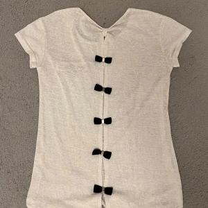 Vit topp med svarta rosetter från M&G Monogram - Krämvit blus med söta detaljer från M&G Monogram i storlek S, använd fåtal gånger så mycket bra skick. Den passar folk som har storlek S💕