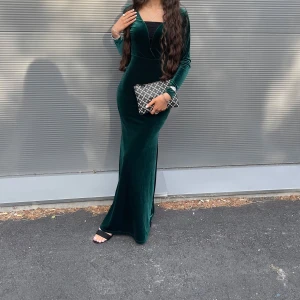 Mörkgrön sammet långklänning - Elegant mörkgrön långklänning i sammet med djup v-ringning och långa ärmar. Perfekt för festliga tillfällen. Klänningen har en tight passform som framhäver figuren.