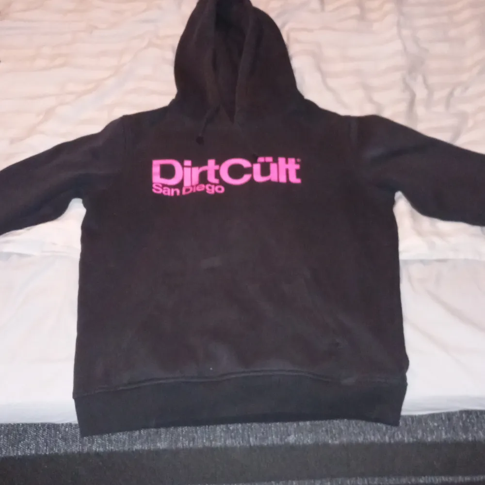 Säljer en svart hoodie från DirtCült med rosa tryck 'San Diego' på bröstet. Den är i bra skick och perfekt för höst och vinter. Hoodien har en klassisk passform med långa ärmar och en mysig huva. Perfekt för chill dagar eller casual häng! 🖤. Hupparit & Collegepaidat.