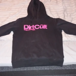 Svart hoodie från DirtCült - Säljer en svart hoodie från DirtCült med rosa tryck 'San Diego' på bröstet. Den är i bra skick och perfekt för höst och vinter. Hoodien har en klassisk passform med långa ärmar och en mysig huva. Perfekt för chill dagar eller casual häng! 🖤