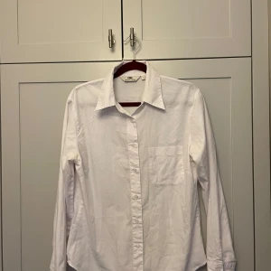 Vit skjorta - Säljer en klassisk vit långärmad skjorta i bomull. Skjortan har en bröstficka och knappar framtill. Den är i mycket bra skick
