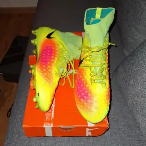 Priset kan diskuteras. Säljer ett par Nike fotbollsskor i grymt skick! De är i en cool neonfärg med inslag av orange och rosa, perfekt för att sticka ut på planen. Skorna har snörning och en hög krage för extra stöd. Sulan har dobbar som ger bra grepp på gräsplaner. Perfekta för fotbollsspelare som vill ha både stil och funktion.