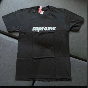 Svart t-shirt från Supreme - Säljer en svart t-shirt från Supreme i nytt skick. Den har en klassisk design med Supreme-loggan tryckt i vitt på framsidan. Perfekt för en casual look eller streetwear-stil. T-shirten är kortärmad och gjord i bomull för en bekväm passform.