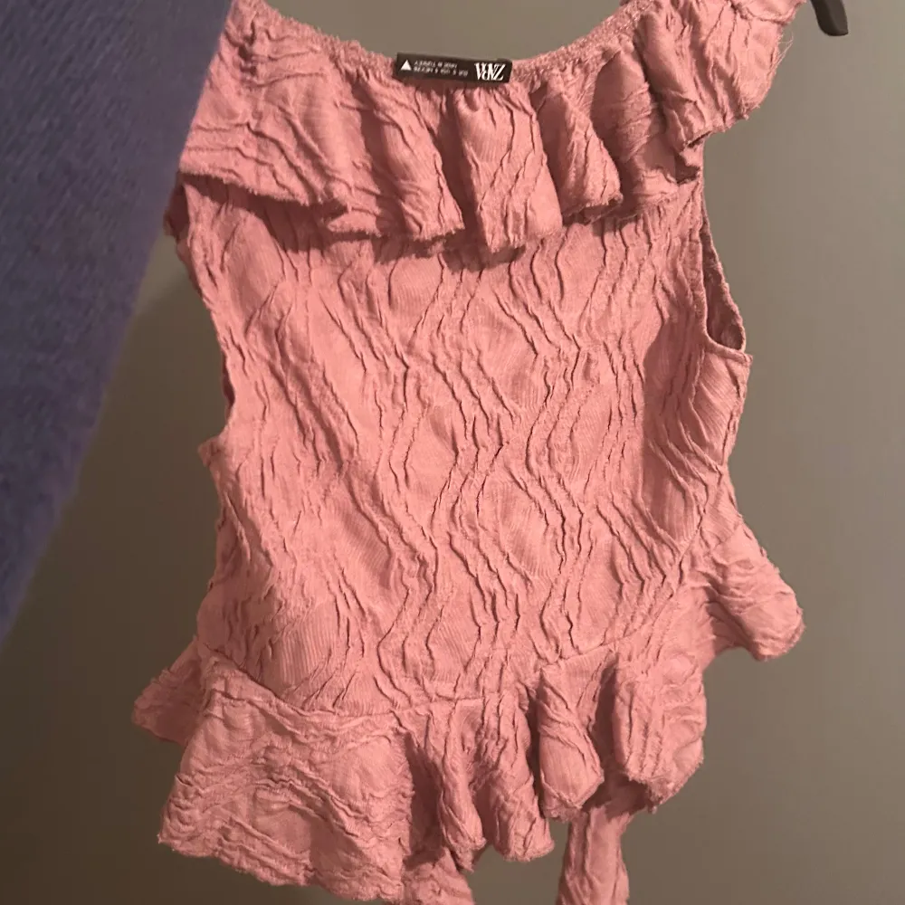 Säljer en superfin rosa topp med volanger. Den är ärmlös och har en v-ringad design som ger en romantisk känsla. Perfekt för sommardagar eller en festlig kväll. Materialet är lätt och luftigt, vilket gör den bekväm att bära. Passar perfekt med jeans eller kjol för en chic look!. Yläosat.