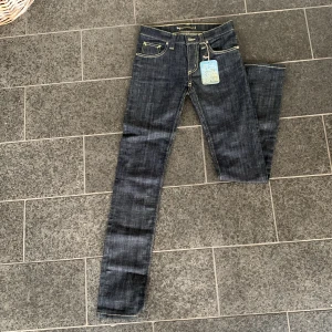 Mörkblå jeans från Denimbirds - Säljer ett par snygga mörkblå jeans från Denimbirds i nytt skick. Low waist storlek; Waist 26, leg 32. De har en klassisk femficksdesign med gul kontrastsöm och en läderpatch med logga baktill. Perfekta för både vardag och fest!