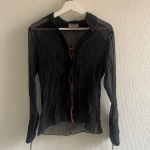 Svart meshblus - Säljer en svart mesh blus från Crazy World i storlek S. Skjortan har långa ärmar och snörning framtill och i ärmarna. Otroligt snygg med bralette under! 🖤