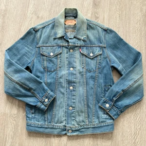 Klassisk jeansjacka från Levi's - Säljer en vintage tidlös jeansjacka från Levi's i storlek M. Jackan har en unik tvätt och klassisk blå denimfärg med knappar fram och två bröstfickor. Perfekt för vår och höst! 🧥