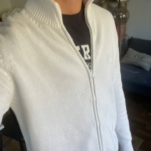 Vit stickad zip-up kofta - Säljer en snygg vit stickad kofta från Marvin&Friends. Den har en dragkedja framtill och en hög krage som håller dig varm. Perfekt för kyliga dagar och passar till det mesta i garderoben. Koftan är i mycket bra skick och redo för en ny ägare!