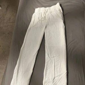 Vita linnebyxor från H&M - Säljer ett par vita linnebyxor från H&M i storlek  XS. De har en bekväm elastisk midja med snörning för perfekt passform. Perfekta för semestrar🤍