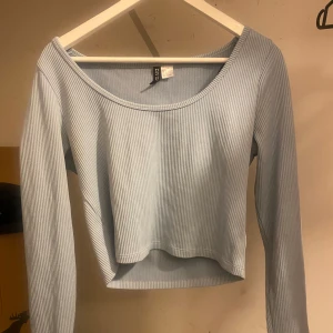 Ljusblå ribbad topp från H&M - Säljer en superfin ljusblå ribbad topp från H&M. Den har långa ärmar och en croppad passform som är perfekt för både vår och sommar. Toppen är i mycket bra skick och passar perfekt till ett par jeans eller kjol.