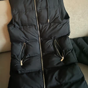 Svart dunväst från Zara - Säljer en svart dunväst från Zara i mycket bra skick. Västen har en dragkedja framtill och två praktiska fickor med dragkedjor. Perfekt för höst för att hålla sig varm. Passar bra till både vardag och lite mer avslappnade tillfällen. Dm om det några frågor! (Inga skador) ( Kan mötas upp i Stockholm)