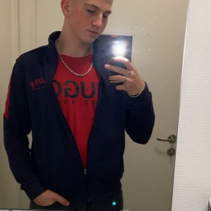 Röd t-shirt från Hugo Boss - Säljer en snygg röd t-shirt från Hugo Boss i storlek M. Den har en klassisk passform med korta ärmar och ett stort Hugo Boss-tryck i svart på framsidan. Perfekt för en casual look eller att ha under en jacka. Skön och stilren, passar till det mesta! ( andra bilden är inte min kom privat för mer bilder) ANDRA BILDEN ÄR LÅNAD 