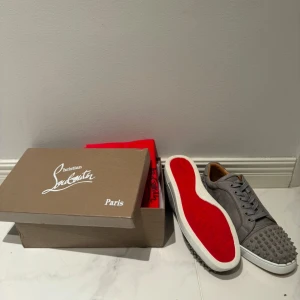 Grå sneakers med nitar från Christian Louboutin - Christian Louboutin skor med alla nitar kvar! Storlek 44 eu. Väldigt fint skick på dessa, allt finns kvar som följer med skorna. Dem har använts en gång!
