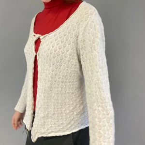 Vit stickad kofta - Säljer en vit stickad kofta med ett fint hålmönster. Koftan har långa ärmar och en enkel knäppning framtill. Perfekt för lager-på-lager-stil.