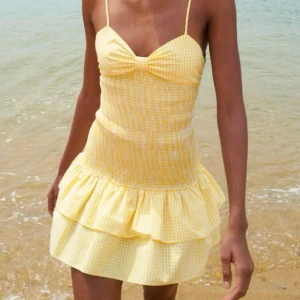 Gul klänning med volang - Gul klänning med smala axelband och volangdetalj i nederkant. Klänningen har en söt rosett i ryggen och en snygg passform.💛helt oanvänd 