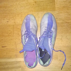 Adidas fotbollsskor med snörning - Säljer ett par Adidas fotbollsskor i vitt och blått med gröna detaljer. Skorna har snörning och dobbar för bra grepp på planen. Perfekta för fotbollsträning och matcher.