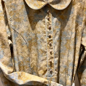 Mönstrad klänning från Beri - Elegant klänning från Beri i storlek 46 med ett vackert mönster i beige och blå toner. Klänningen har långa ärmar och knappar framtill samt ett matchande bälte i midjan. Perfekt för en stilfull look.