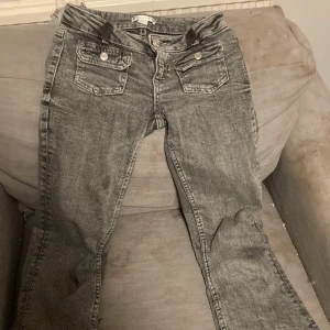 Grå jeans med fickdetaljer - Snygga grå jeans med två framfickor med knappar. De har en klassisk design med en rak passform och är perfekta för en avslappnad stil. Jeansen har en dragkedja och knappstängning.