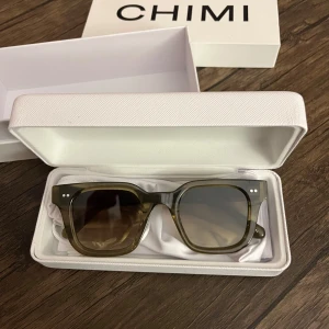 Solglasögon från CHIMI - Snygga solglasögon från CHIMI med en fyrkantig form och transparent brun färg. De har en stilren design med två små vita prickar på bågarna. Perfekta för att ge en cool touch till din stil. Säljer mina chimi glasögon då jag inte får användning för dem💕 i bra skick, de ända är att den vita påsen har en fläck på sig ( kan skicka bild vid intresse) annars väldigt fint skick! 💚Skickas i orginalförpackning!
