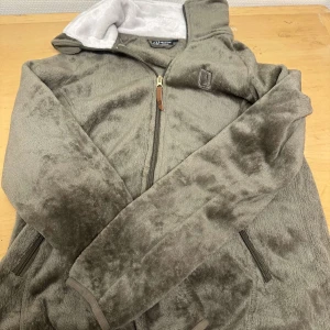 Brun fleecejacka från Jacson - Mysig brun fleecejacka från Jacson med dragkedja framtill. Jackan har en hög krage och långa ärmar, perfekt för kyliga dagar. Den är tillverkad i mjukt fleecematerial och har praktiska fickor med dragkedja.