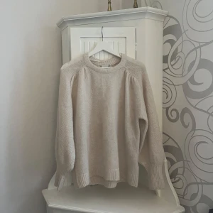 Beige stickad tröja från ICHI - Mysig beige stickad tröja från ICHI med rund halsringning och långa ärmar. Perfekt för kyligare dagar med sin mjuka och bekväma passform. Ribbstickade muddar vid ärmslut och nederkant ger en stilren look.