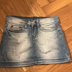 Lowwaist Vintage blå minikjol med slitningar - Snygg blå jeanskjol från Tally Weijl i. Kjolen har fina fickor och små slitningar på framsidan, samt en liten ficka med nitar på