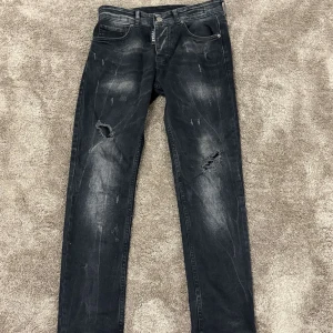 Svarta jeans från ICON2 - Snygga svarta jeans från ICON2 med slitna detaljer och hål på benen. De har en klassisk femficksdesign och knappgylf. Perfekta för en avslappnad stil med en edgy touch.