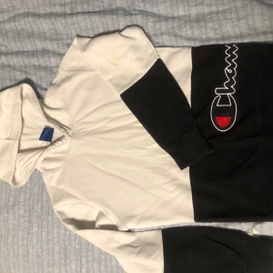 Vit och svart hoodie från Champion - Säljer en snygg vit och svart hoodie från Champion. Tröjan har en stor logga på framsidan och är tillverkad i mjukt material. Perfekt för en avslappnad stil.