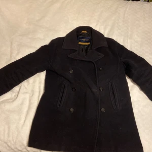 Svart skepparkavaj från Henri Lloyd - Snygg svart skepparkavaj från Henri Lloyd i storlek M. Jackan har en klassisk dubbelknäppt design med bred krage och långa ärmar. Perfekt för kyligare dagar med sin stilrena look.
