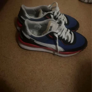 Blå sneakers från Puma - Snygga blå sneakers från Puma med vita och röda detaljer. Skorna har en klassisk snörning och en bekväm sula. Perfekta för en sportig look.