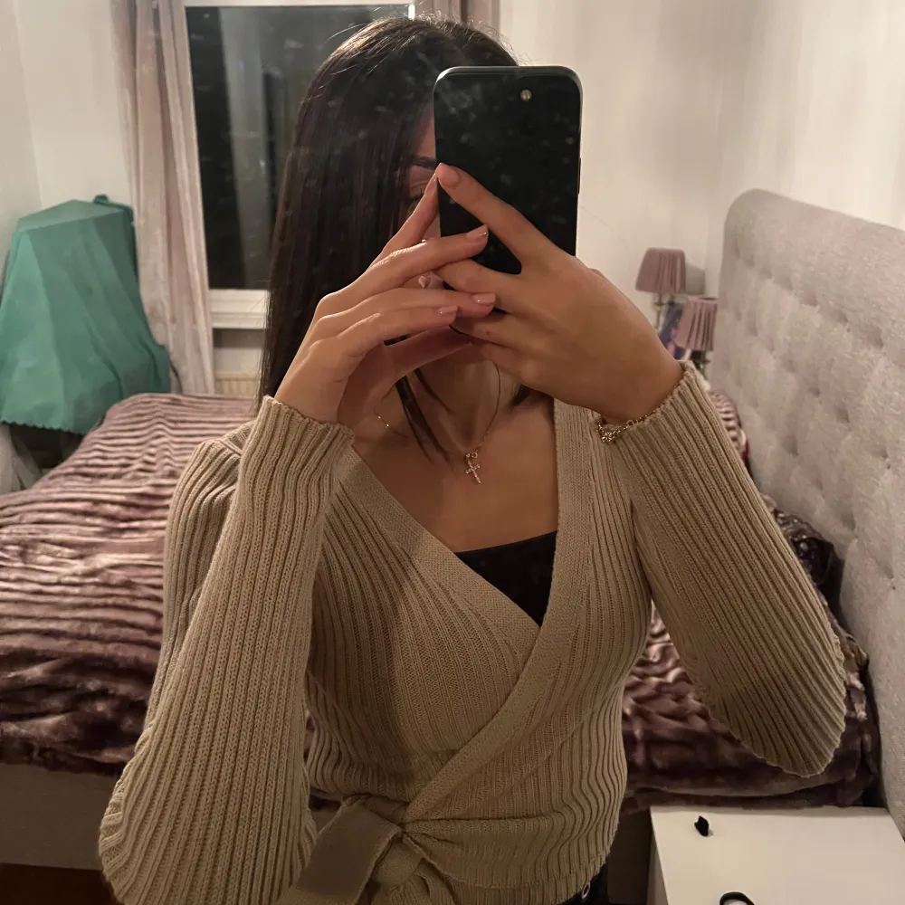 Säljer en snygg beige ribbad omlottkofta med knytning i midjan. Koftan har långa ärmar och en v-ringad design.. Neuletakit & Villapaidat.