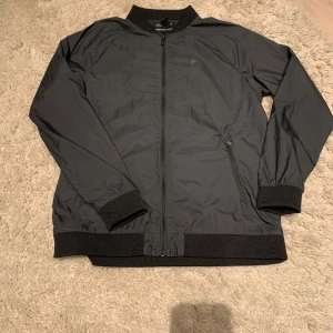 Svart vindjacka från Peak Performance - Snygg svart windbreaker från Peak Performance med dragkedja. Jackan har två praktiska fickor med dragkedja och en stilren design som passar perfekt för blåsiga dagar. Hör av er vid frågor!!