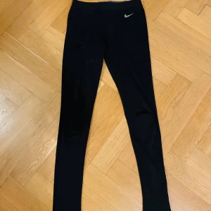 Svarta träningstights från Nike - Snygga svarta träningstights från Nike med en liten logga på vänster höft. Perfekta för träning eller en avslappnad dag. De är stretchiga och bekväma med en tight passform.